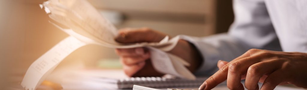 Close-up of economist using calculator while going through bills and taxes in the office.