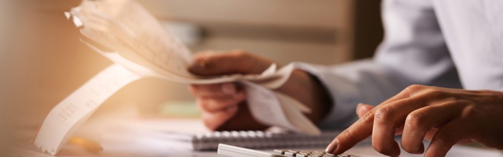 Close-up of economist using calculator while going through bills and taxes in the office.