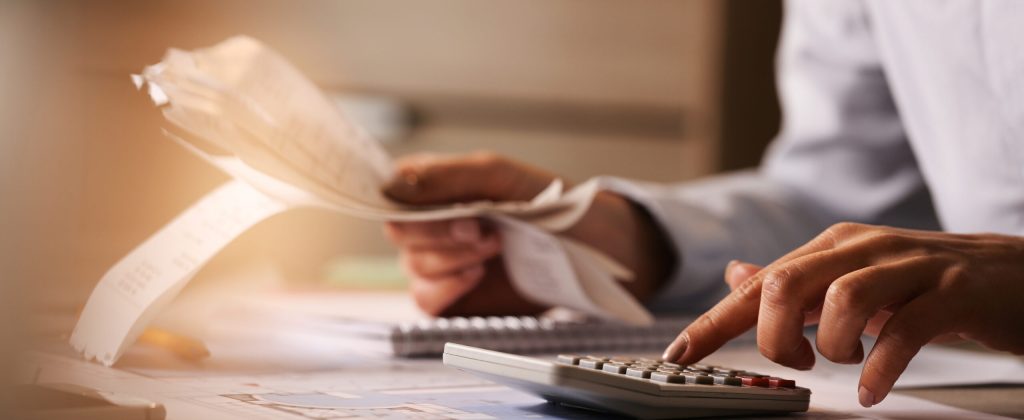 Close-up of economist using calculator while going through bills and taxes in the office.
